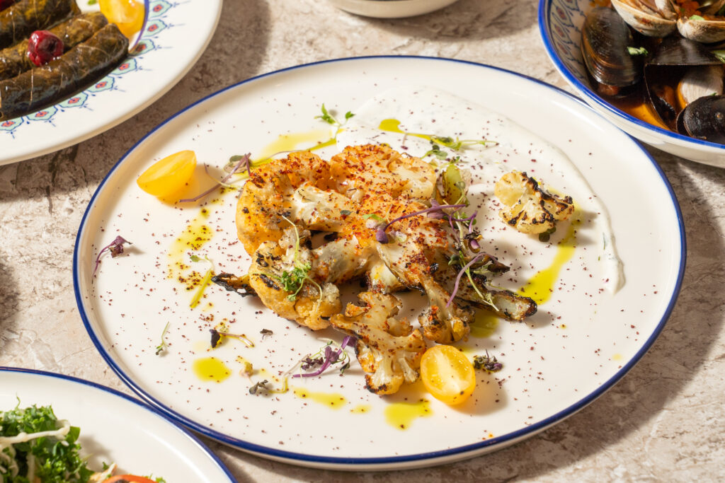 Close-up of a golden roasted cauliflower steak with yellow tomatoes at Olivea Restaurant