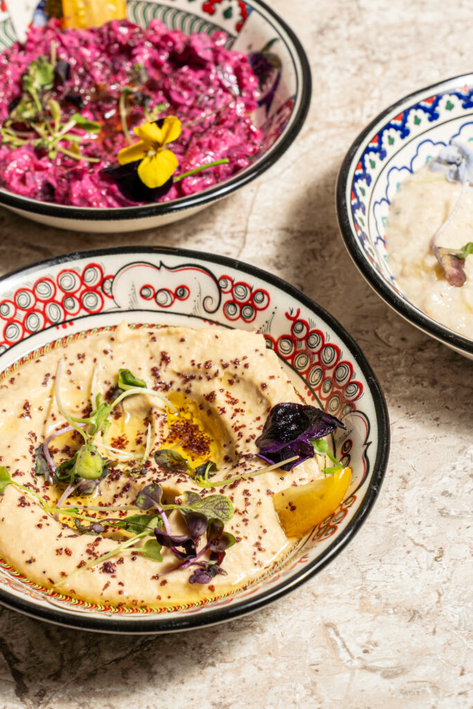 Hummus garnished with herbs and edible flowers beside other mezze dips at Olivea Restaurant